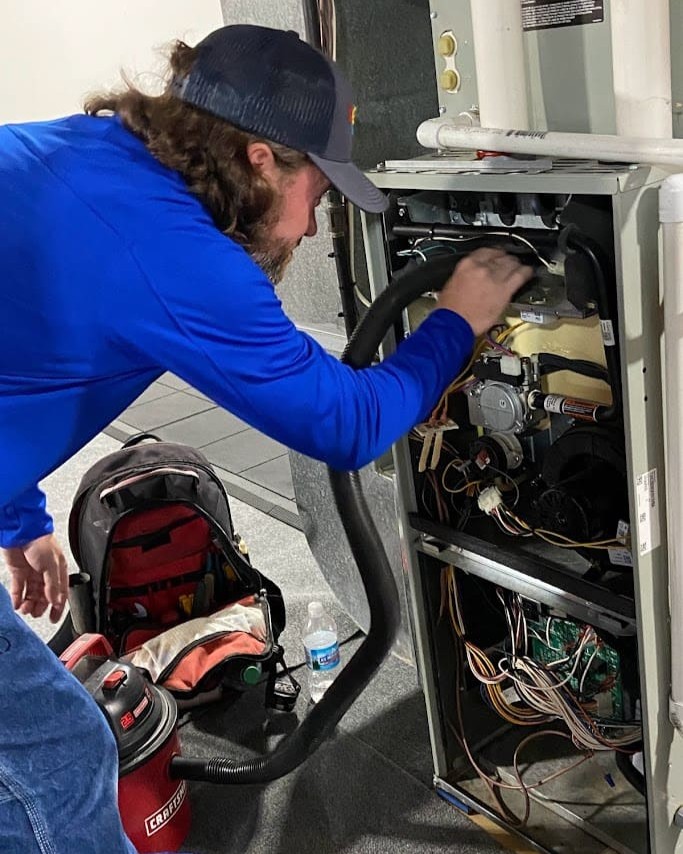 Logan Services HVAC technician cleaning furnace during maintenance appointment.
