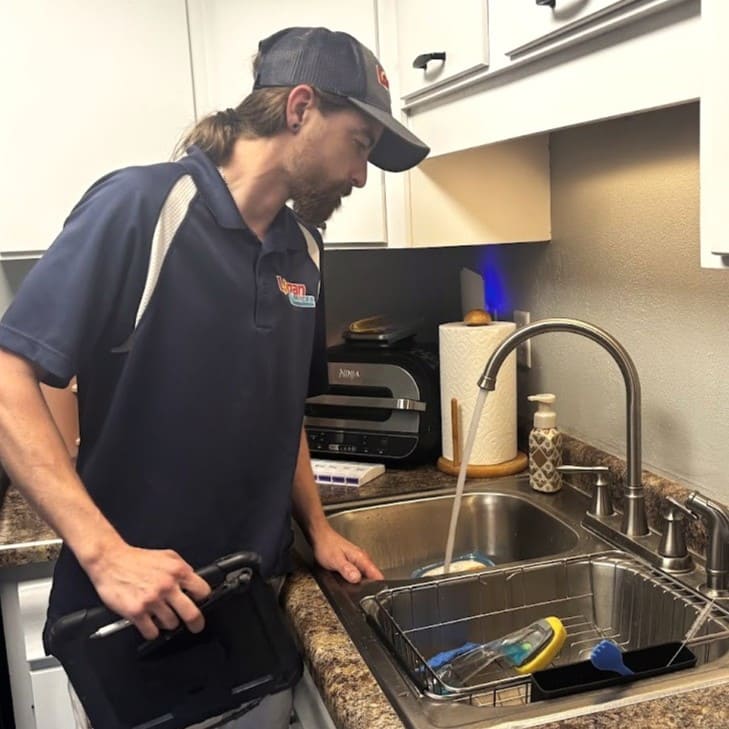 Logan Services plumber inspecting kitchen sink for water pressure issues.