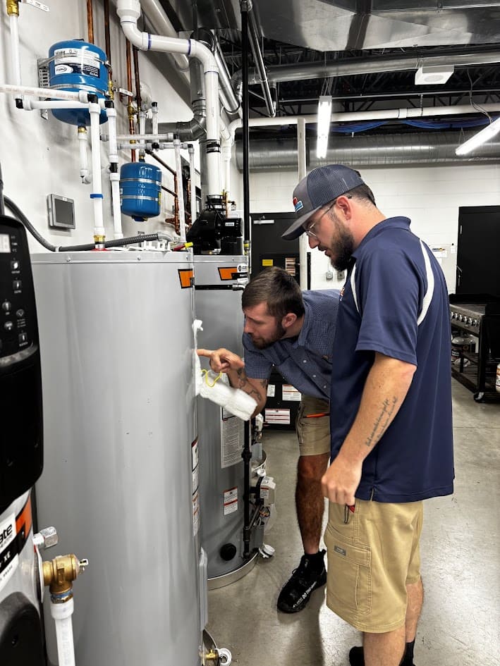 Logan Services plumbers working on a standard water heater in the training center.