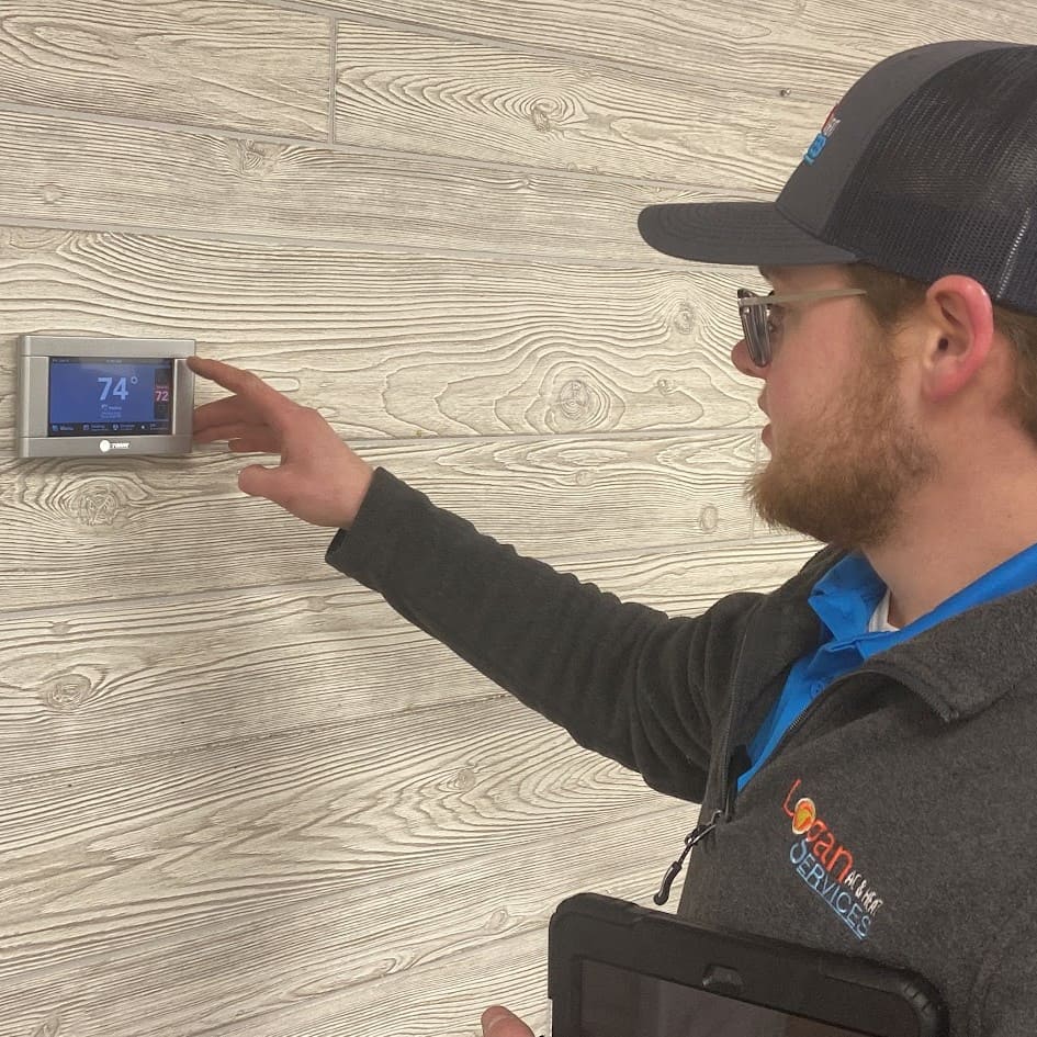 Logan Services HVAC technician adjusting thermostat after furnace tune-up.